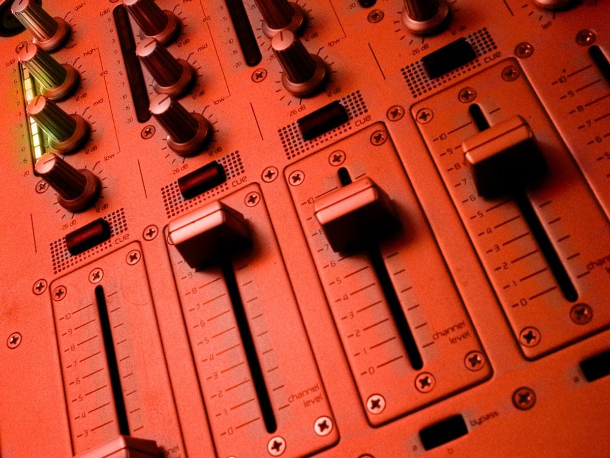 Faders van een dj-mengpaneel, uitgelicht in fel rood licht.